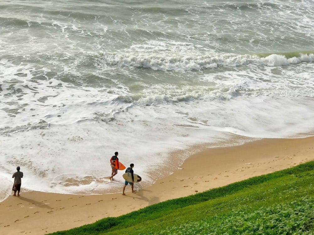Students walking along a Brazilian beach with surfboards, showing a coastal lifestyle during a school exchange in Brazil.