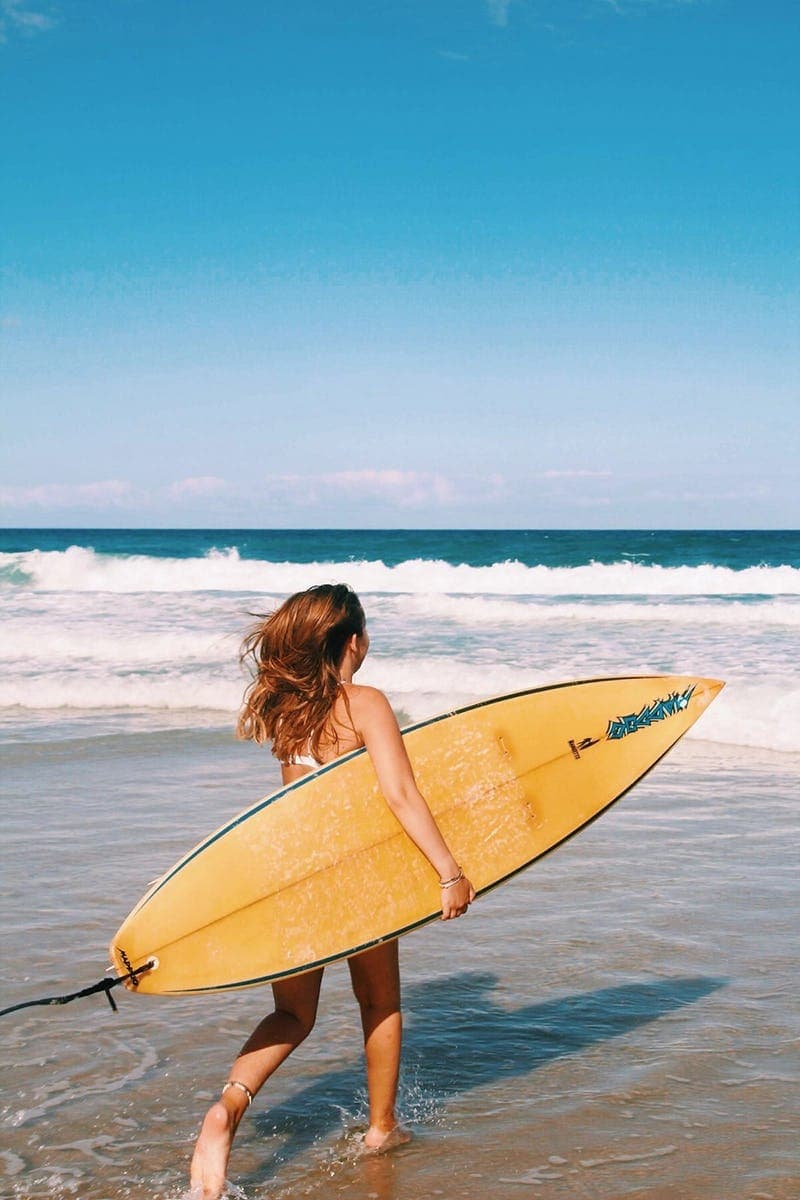 Student on the beach with a surfboard during a year abroad, balancing school life and leisure in Australia.
