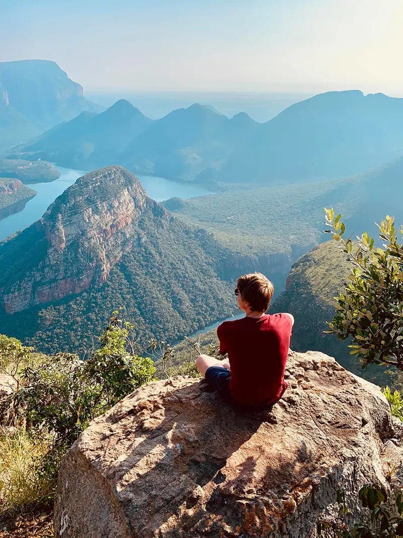 A boy sitting on a rock, admiring the breathtaking views of mountains and valleys in South Africa, as part of his school exchange programme.