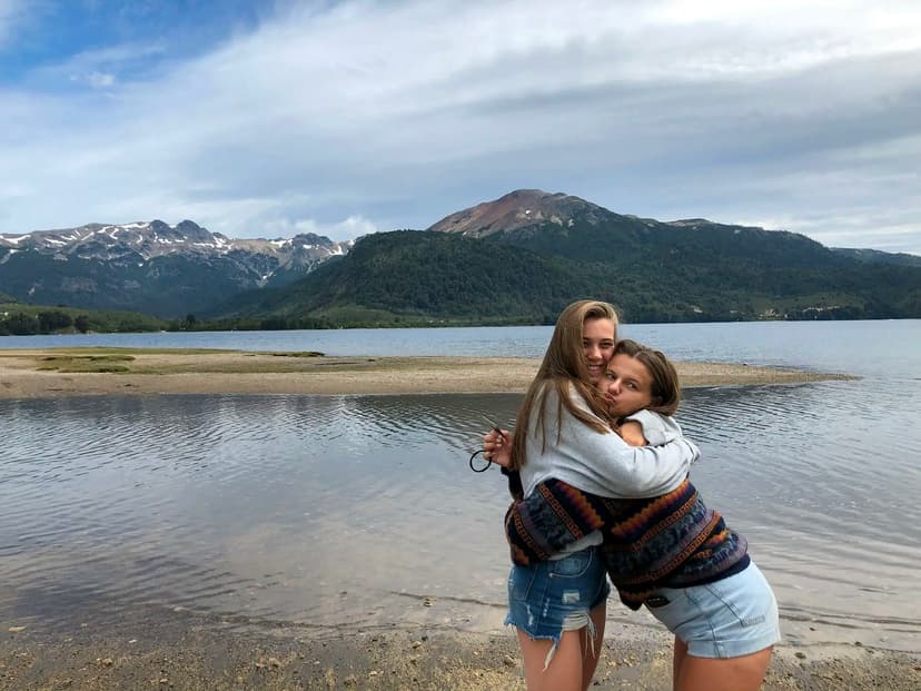 Two students hugging by a lake and mountains, representing friendships and personal bonds built during a school programme in Argentina.