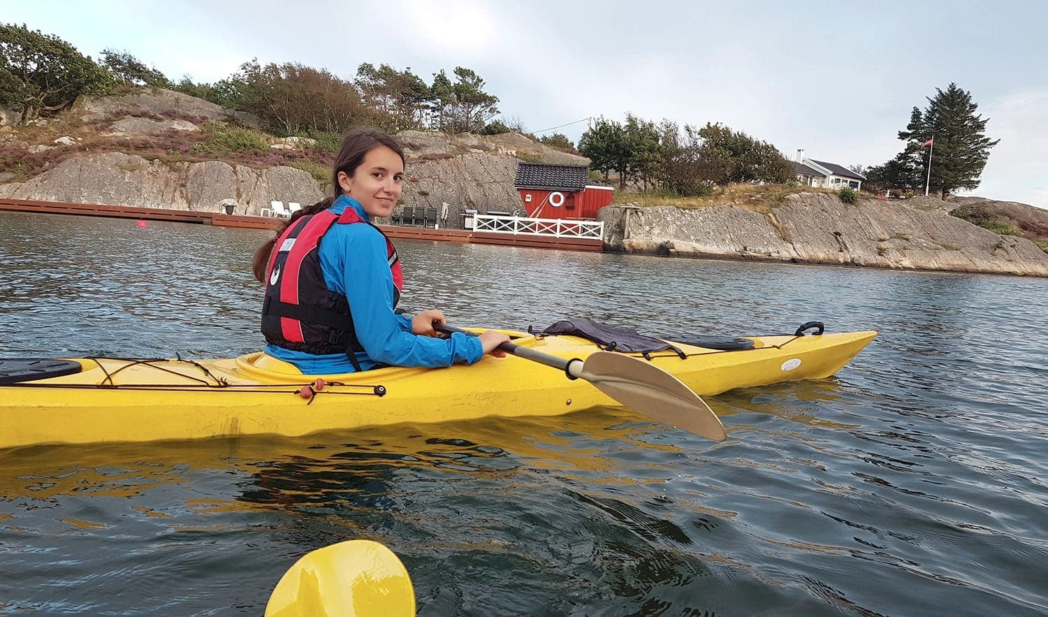 A young woman kayaking in the Norwegian waters, fully immersed in the outdoor adventure of Norway during her school exchange year.