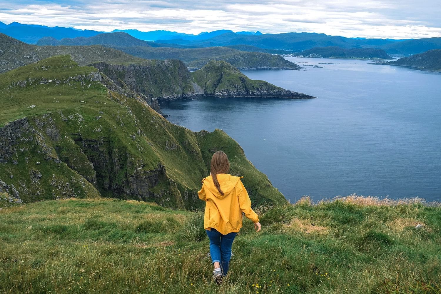 A young woman walking through a Norwegian mountain landscape, taking in the breathtaking view of the sea and mountains, experiencing an unforgettable adventure during her school exchange programme in Norway.