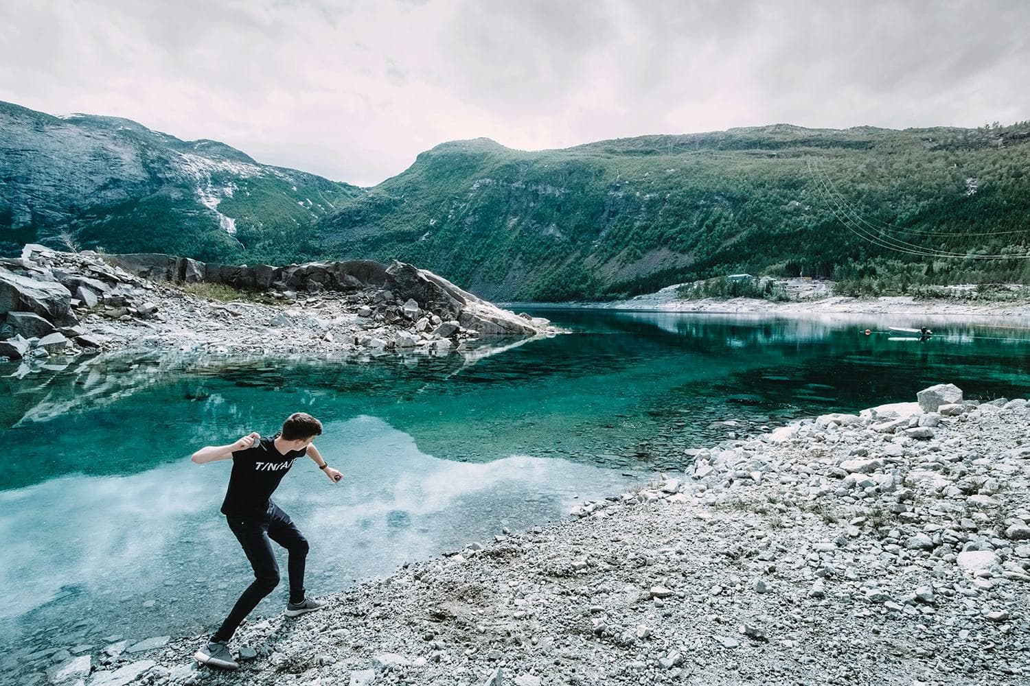 A young man exploring the Norwegian mountain landscape, crossing rocky terrain by a crystal-clear lake, experiencing an outdoor adventure during his school exchange year.