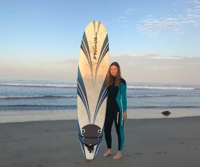 Student in a wetsuit with a surfboard on an American beach, illustrating everyday life during a USA school exchange programme.