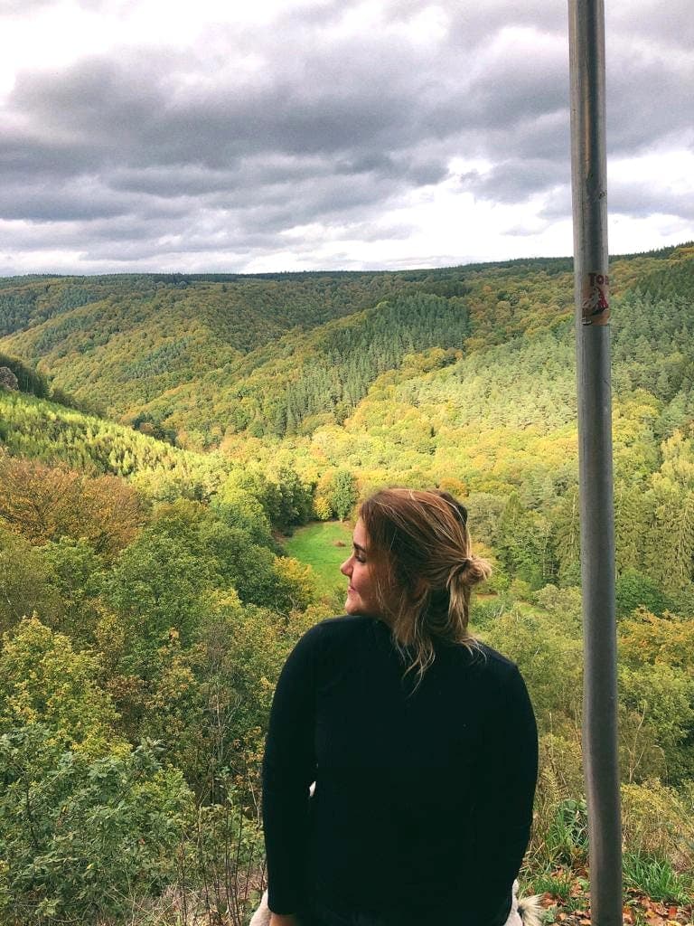 Student contemplating the natural landscape of Belgium during their study year abroad, surrounded by green hills.