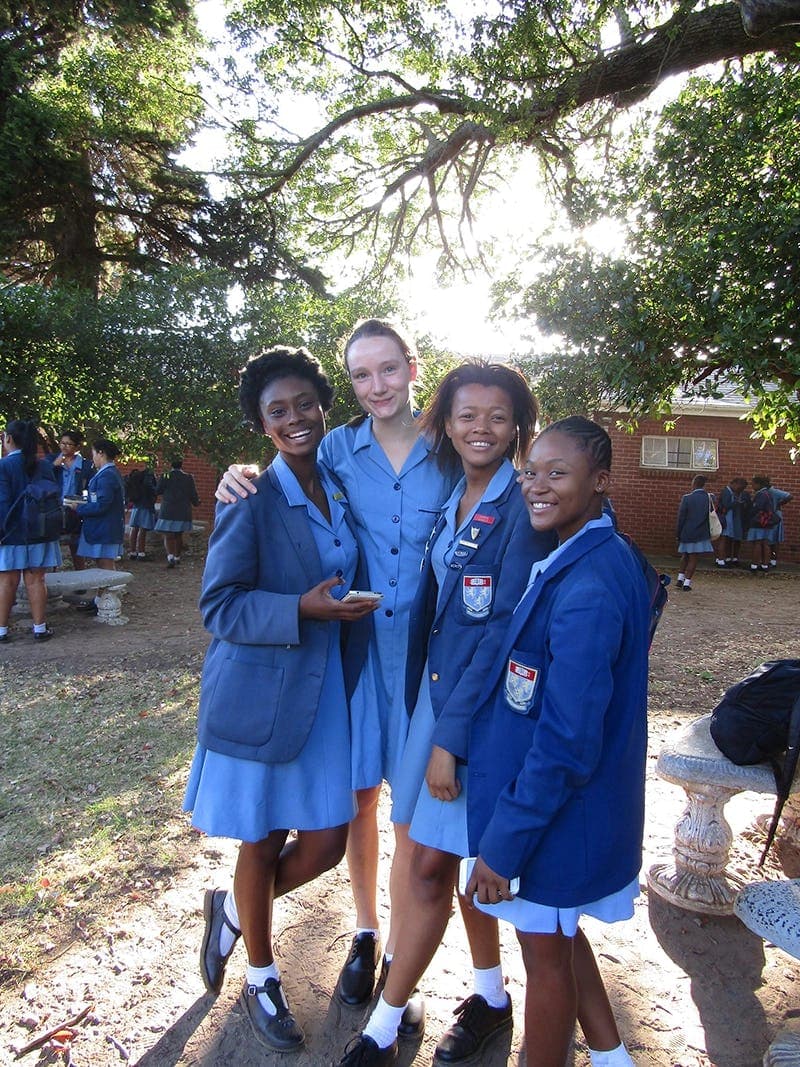 Four girls smiling together in the schoolyard in South Africa, experiencing a unique cultural exchange and friendships during their school exchange programme in South Africa.