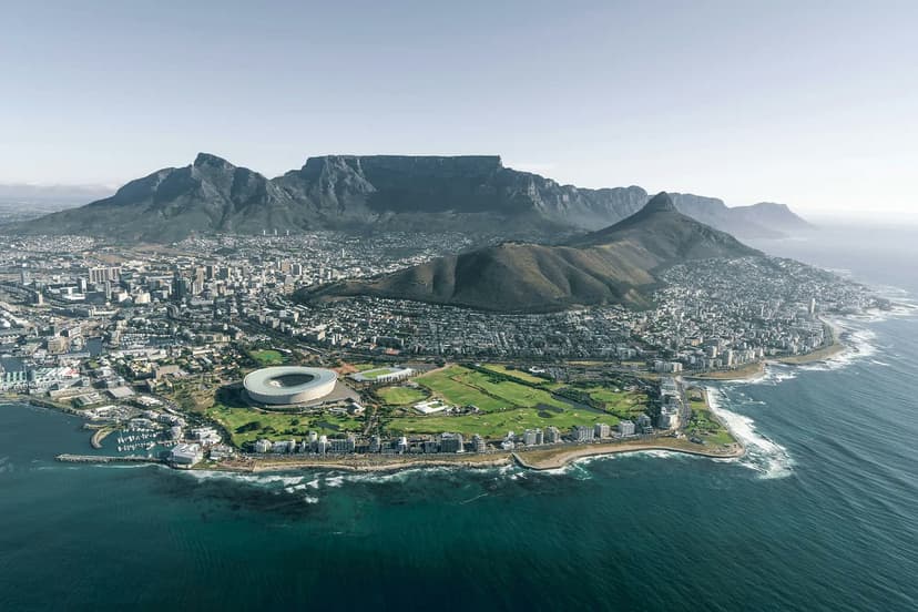 A stunning view of Cape Town, with Table Mountain towering over the city and the Olympic Stadium visible along the South African coastline.