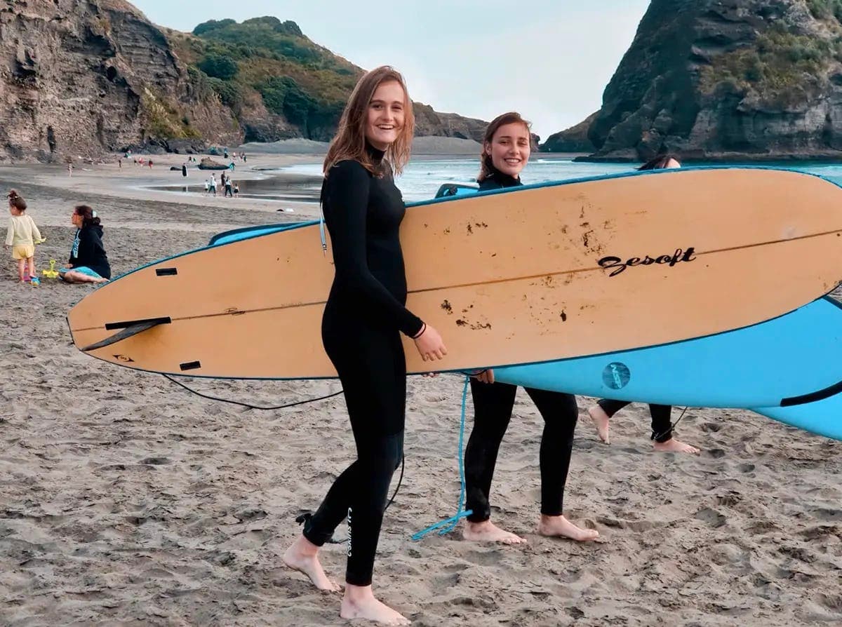 Smiling students surfing on the beach, living a unique educational experience during the school year in New Zealand.