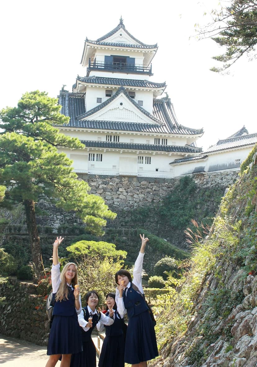 Students in uniform in front of a traditional Japanese castle during a high school programme in Japan, experiencing school life.