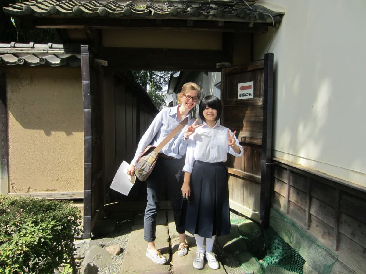 International student with a Japanese student outside a traditional school, taking part in a school exchange programme in Japan.